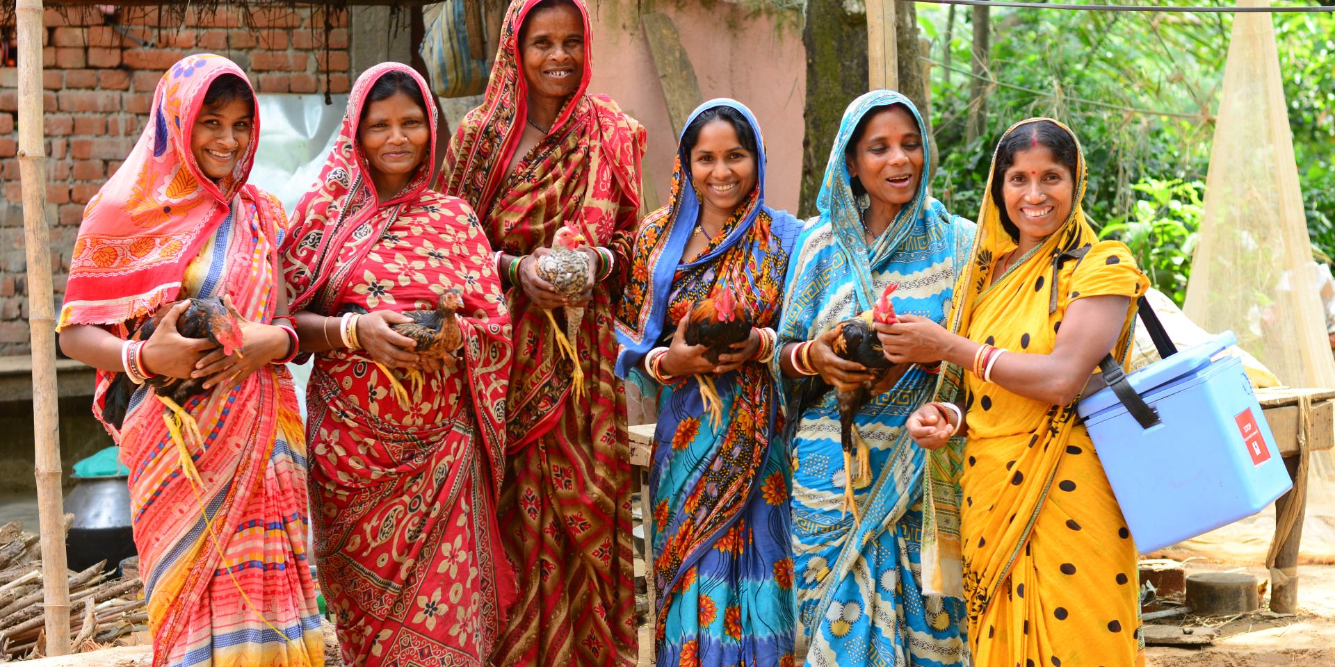 A group of six women standing outdoors, smiling and holding chickens.