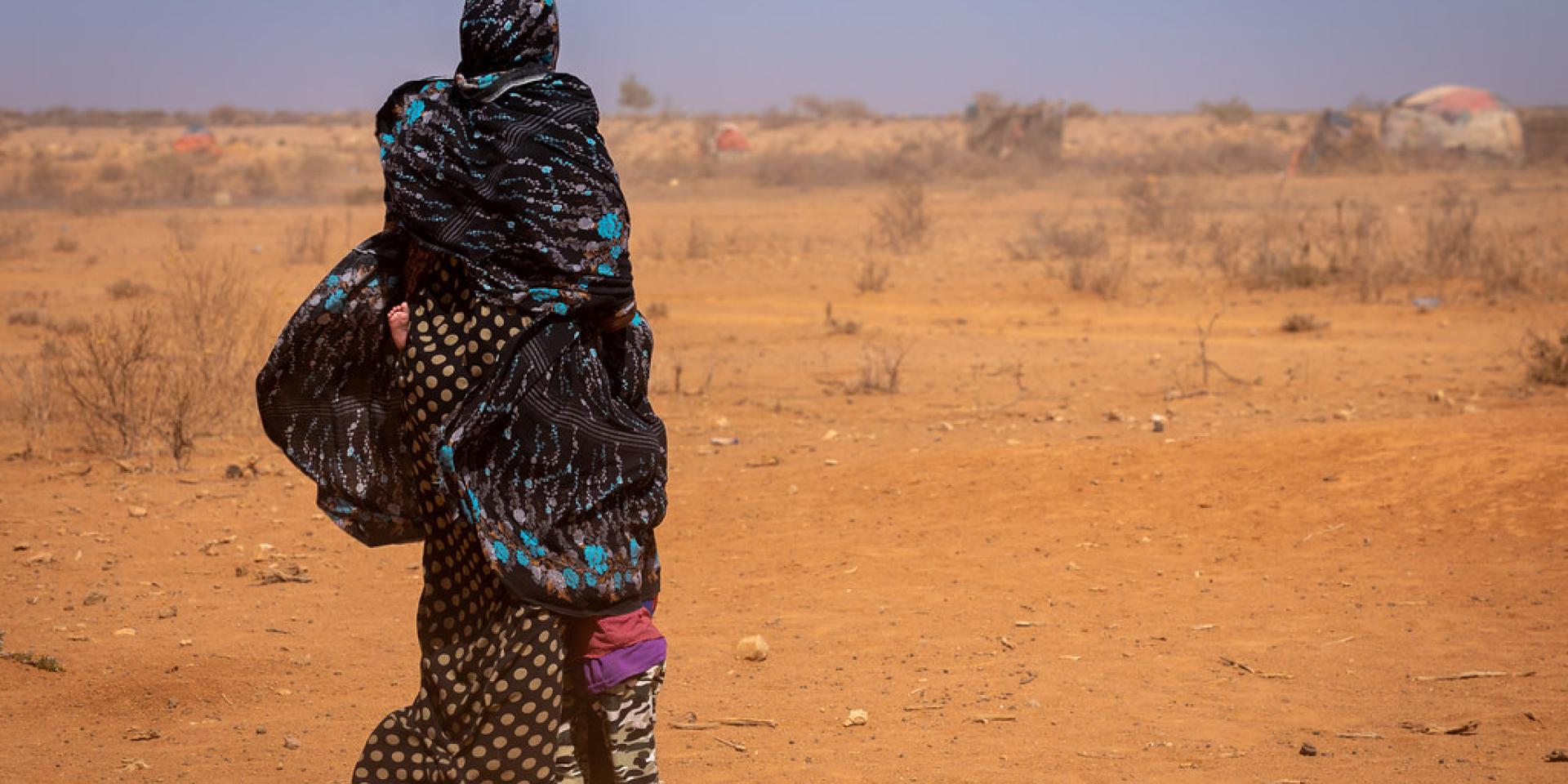 Drought in Ethiopia. A woman holding her child with dry landscape in the background